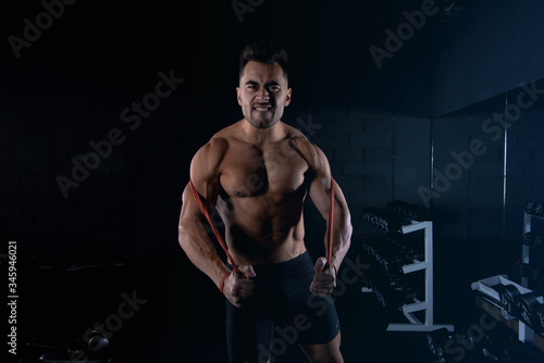 male athlete squeezes muscles with elastic band gym, sexy guy bodybuilder, sports lifestyle, home sport. © Oleh