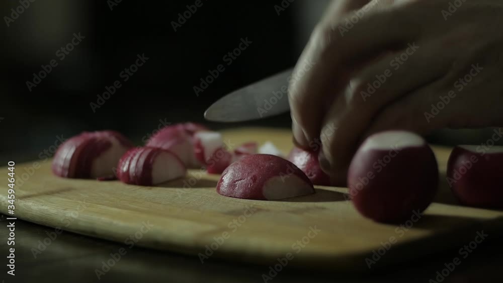 close up cutting radishes on a wooden Board on a dark background with men's hands close up cutting radishes on a wooden Board on a dark background with men's hands