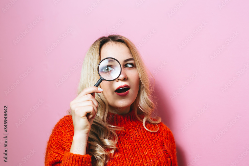 Portrait of a beautiful pretty blonde girl looking through magnifying glass isolated over pink background Portrait of a beautiful pretty blonde girl looking through magnifying glass isolated over pink background