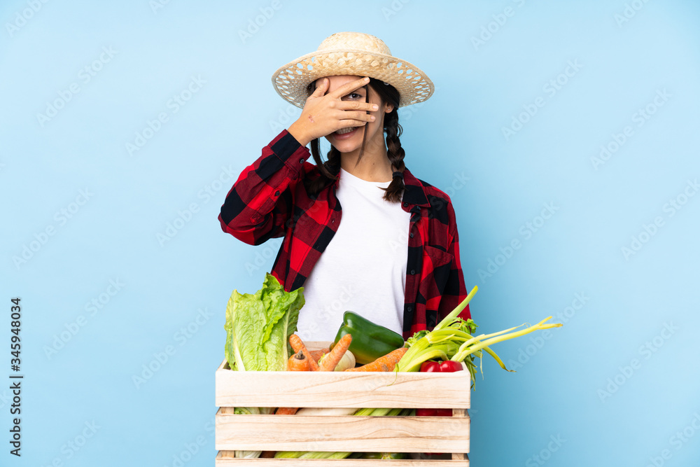 Young farmer Woman holding fresh vegetables in a wooden basket covering eyes by hands and smiling
