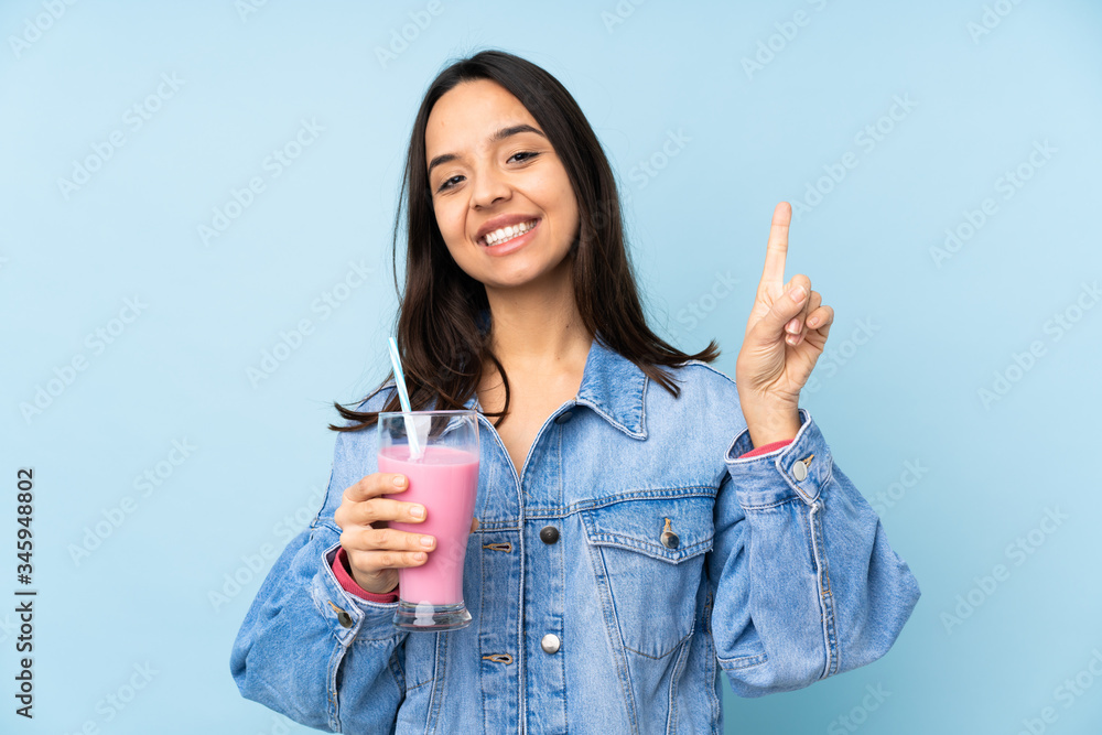 Young woman with strawberry milkshake over isolated blue background showing and lifting a finger in sign of the best