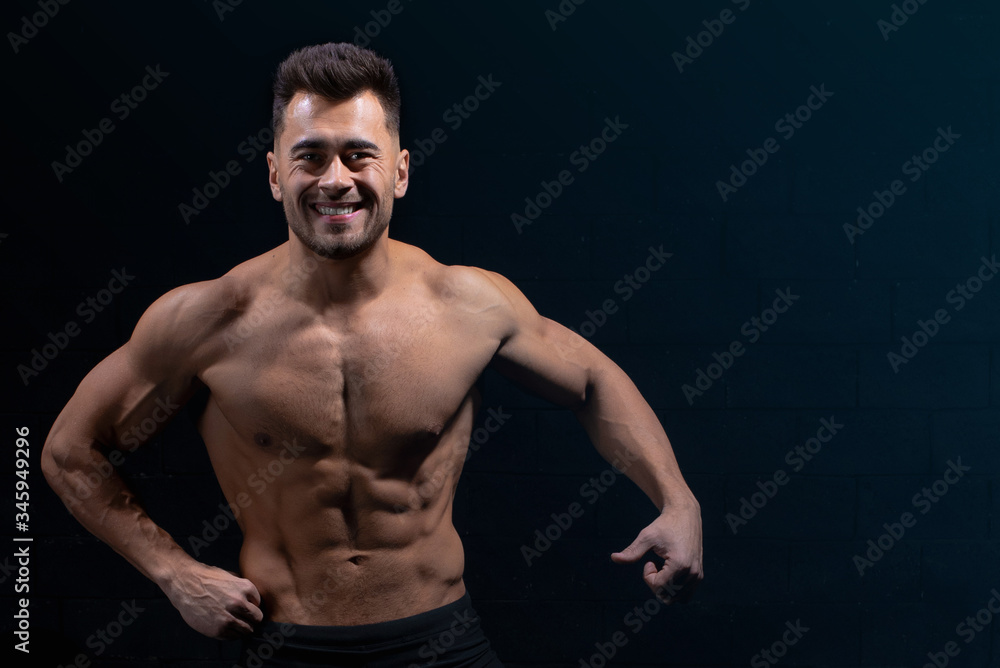 male athlete shows body and muscles on dark wall background in gym, sexy guy bodybuilder, sports lifestyle, home sport.