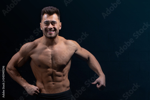 male athlete shows body and muscles on dark wall background in gym, sexy guy bodybuilder, sports lifestyle, home sport.