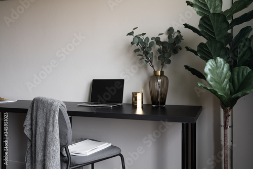 Fototapeta Naklejka Na Ścianę i Meble -  Bedroom working corner decorated with laptop, white candles and artificial plant in glass vase on black wood  working table with beige painted wall in the background /apartment interior / copy space
