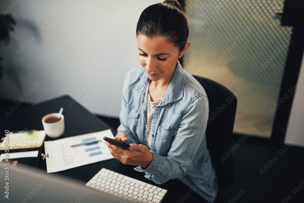 Businesswoman reading a text on her cellphone in an office Businesswoman reading a text on her cellphone in an office