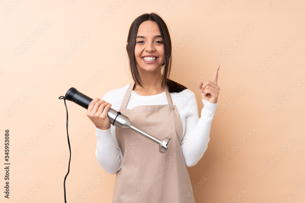 Young brunette girl using hand blender over isolated background pointing up a great idea Young brunette girl using hand blender over isolated background pointing up a great idea