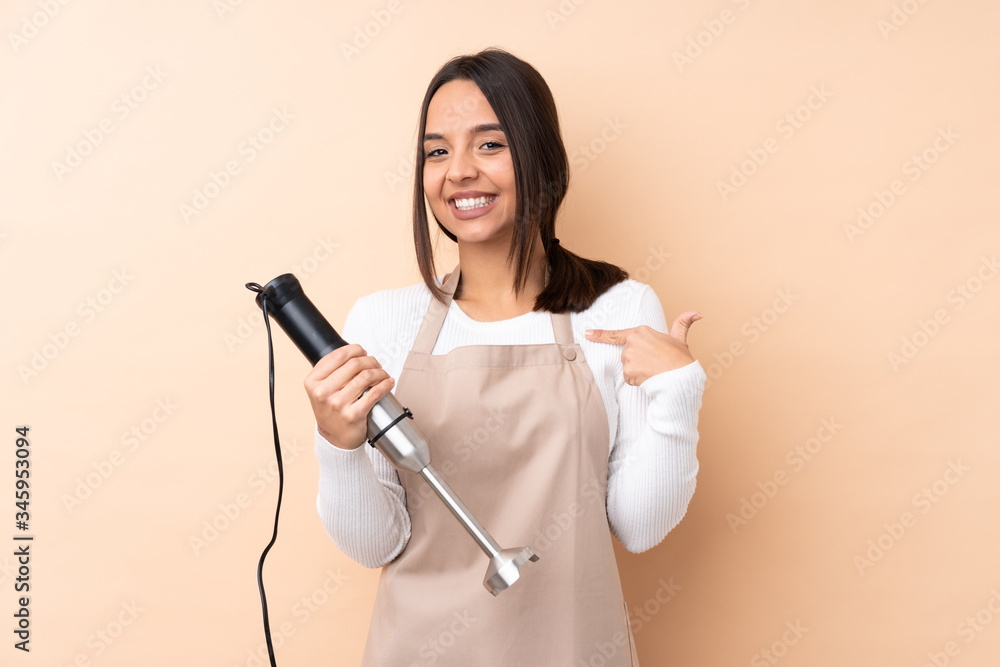 Young brunette girl using hand blender over isolated background proud and self-satisfied Young brunette girl using hand blender over isolated background proud and self-satisfied