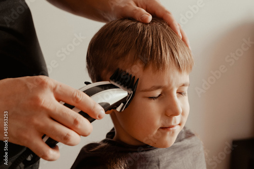 Kid boy getting a haircut at home. A boy with a dissatisfied face