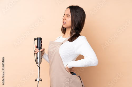 Young brunette girl using hand blender over isolated background suffering from backache for having made an effort