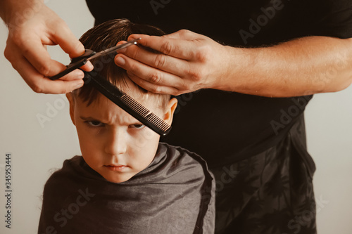 A father cuts his son's hair with scissors at home. A boy with a emotional face