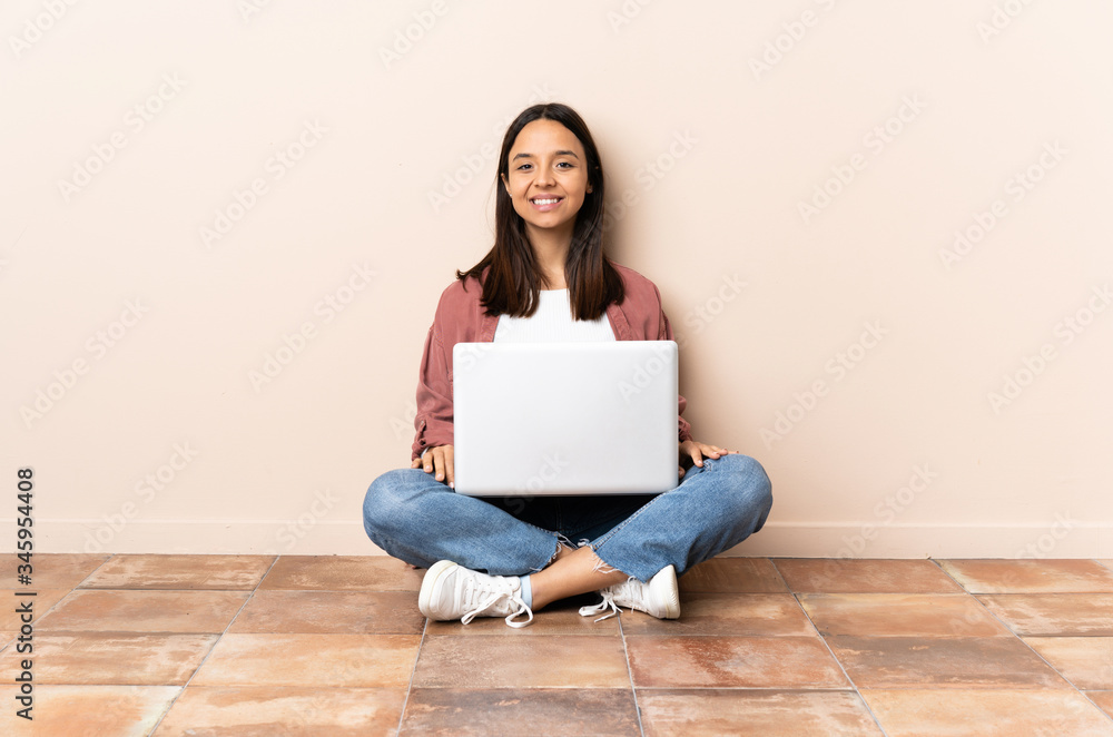 Young mixed race woman with a laptop sitting on the floor laughing Young mixed race woman with a laptop sitting on the floor laughing