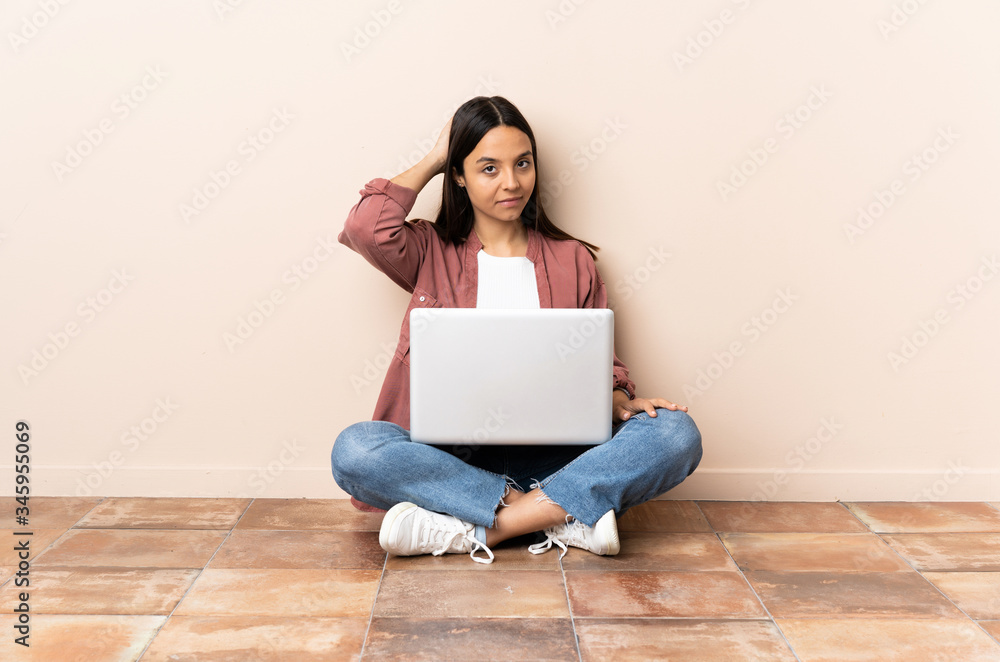 Young mixed race woman with a laptop sitting on the floor in back position and thinking