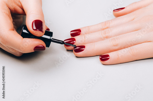 Woman making red manicure by herself on grey background.