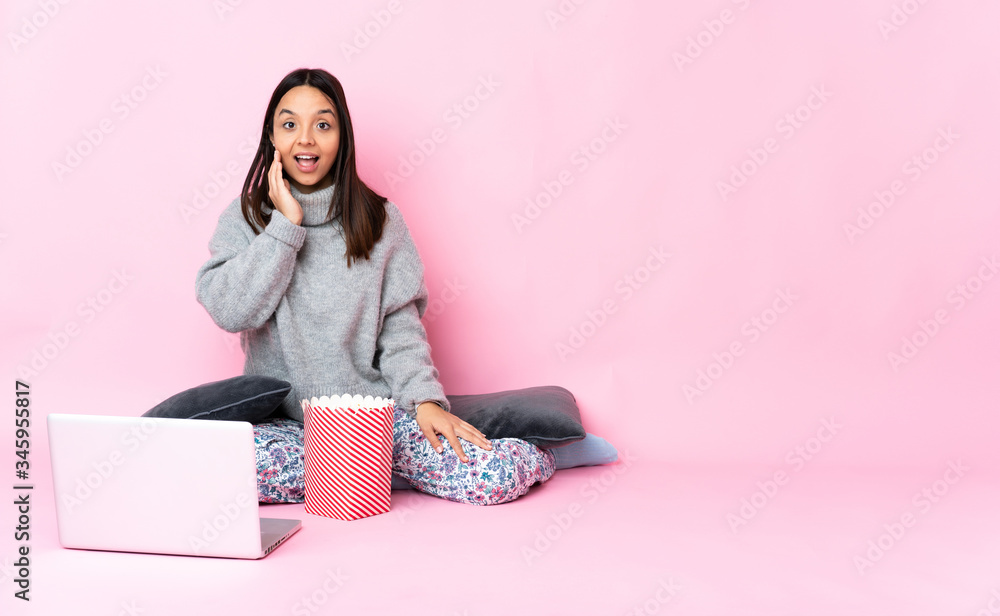 Young mixed race woman eating popcorn while watching a movie on the laptop with surprise and shocked facial expression Young mixed race woman eating popcorn while watching a movie on the laptop with surprise and shocked facial expression
