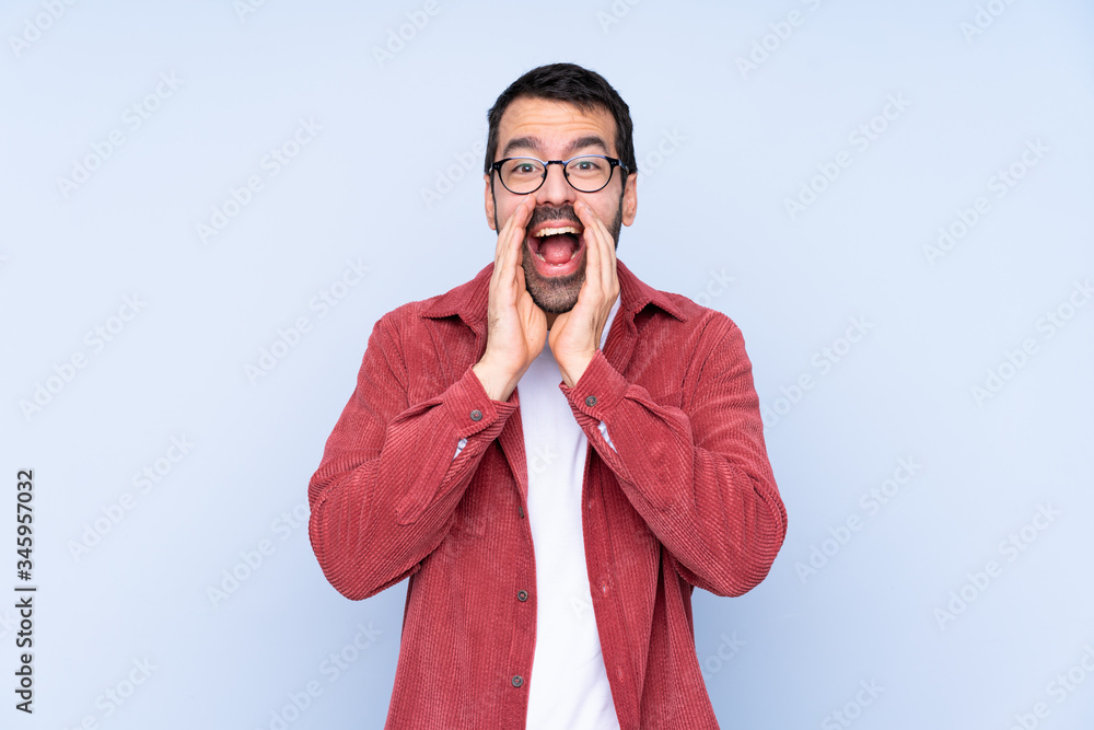 Young caucasian man wearing corduroy jacket over blue background shouting and announcing something Young caucasian man wearing corduroy jacket over blue background shouting and announcing something