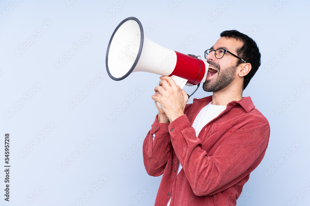 Young caucasian man wearing corduroy jacket over blue background shouting through a megaphone Young caucasian man wearing corduroy jacket over blue background shouting through a megaphone