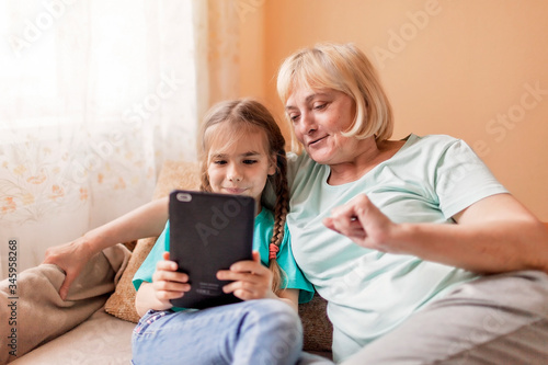 Happy grandchild teaching her grandma to use portative tablet and make selfie, new normal