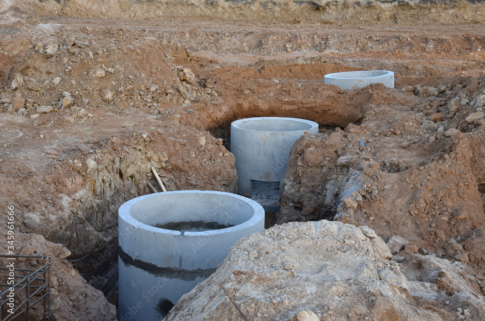 Laying concrete manholes and heating drain pipes and for stormwater system in trench at construction site. Sewerage manhole and pipes line under construction. Chambers and Pump Station Laying concrete manholes and heating drain pipes and for stormwater system in trench at construction site. Sewerage manhole and pipes line under construction. Chambers and Pump Station