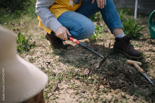 Cropped woman digging the soil using fork and mattock