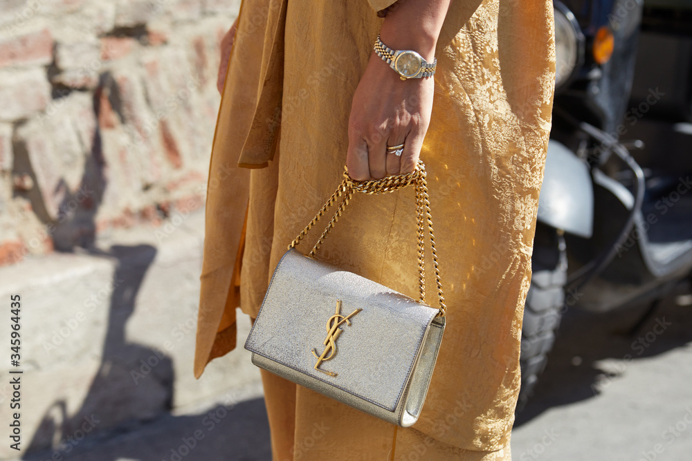 Woman with golden dress, silver Yves Saint Laurent bag and Rolex watch on  September 21, 2019 in Milan, Italy Stock-Foto | Adobe Stock