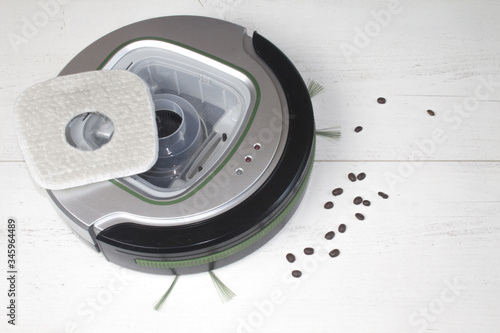 Automatyczny odkurzacz na białych panelach podłogowych, który sprząta ziarna kawy i inne zanieczyszczenia wymagające codziennego czyszczenia.

