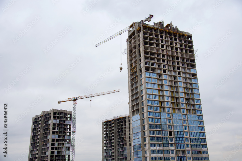 Tower cranes working at construction site against blue sky. Crane lifting a concrete bucket. Construction process of the new residential buildings. Transportation blocks and pouring of the cement mix Tower cranes working at construction site against blue sky. Crane lifting a concrete bucket. Construction process of the new residential buildings. Transportation blocks and pouring of the cement mix