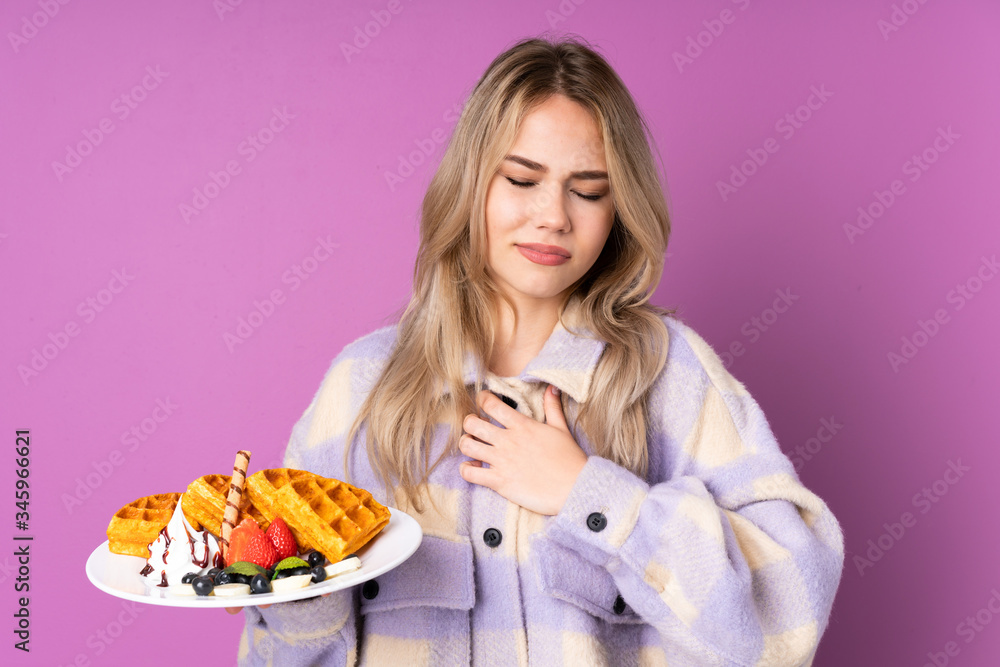 Teenager Russian girl holding waffles isolated on purple background having a pain in the heart Teenager Russian girl holding waffles isolated on purple background having a pain in the heart