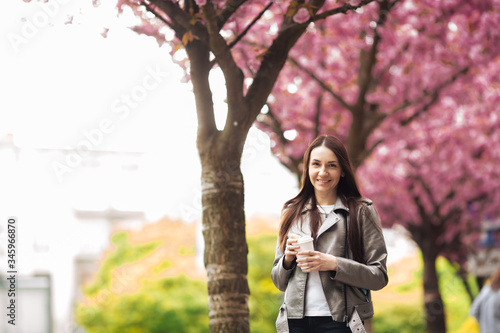 Woman in good mood posing with cup of coffee against sakura tree