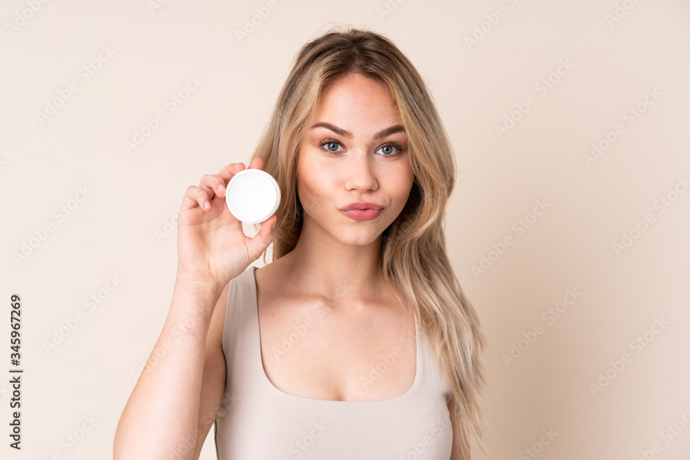 Teenager blonde girl with moisturizer over isolated background Teenager blonde girl with moisturizer over isolated background