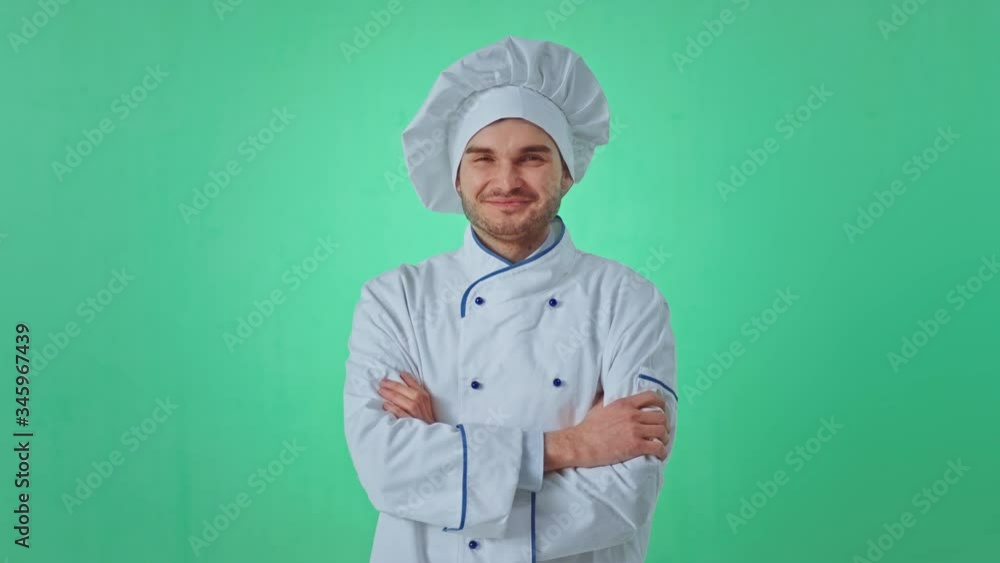 Attractive baker man posing in front of the camera crossing hands inside of a green studio he have a large smile Attractive baker man posing in front of the camera crossing hands inside of a green studio he have a large smile