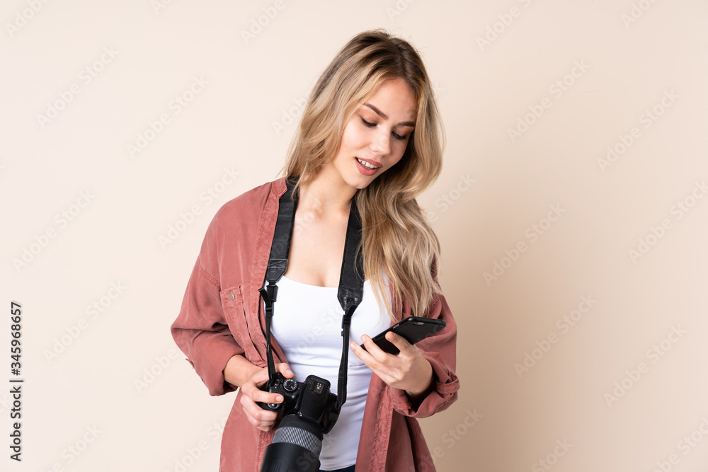 Young photographer girl over isolated background sending a message with the mobile Young photographer girl over isolated background sending a message with the mobile
