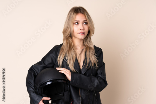 Russian girl with a motorcycle helmet isolated on beige background with confuse face expression © luismolinero
