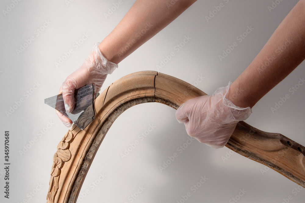 Obraz premium Removing the old paint and varnish with a piece of glass from furniture. Renovation of old furniture as an antique Victorian old wooden armchair.