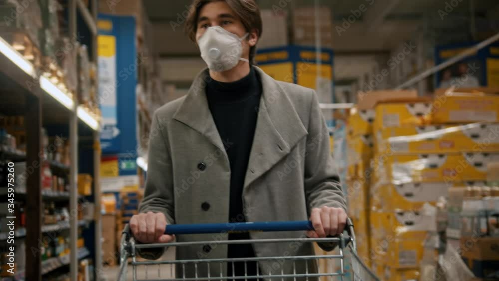 Young man in protective mask and grey coat pushing the pushcart Young man in protective mask and grey coat pushing the pushcart
