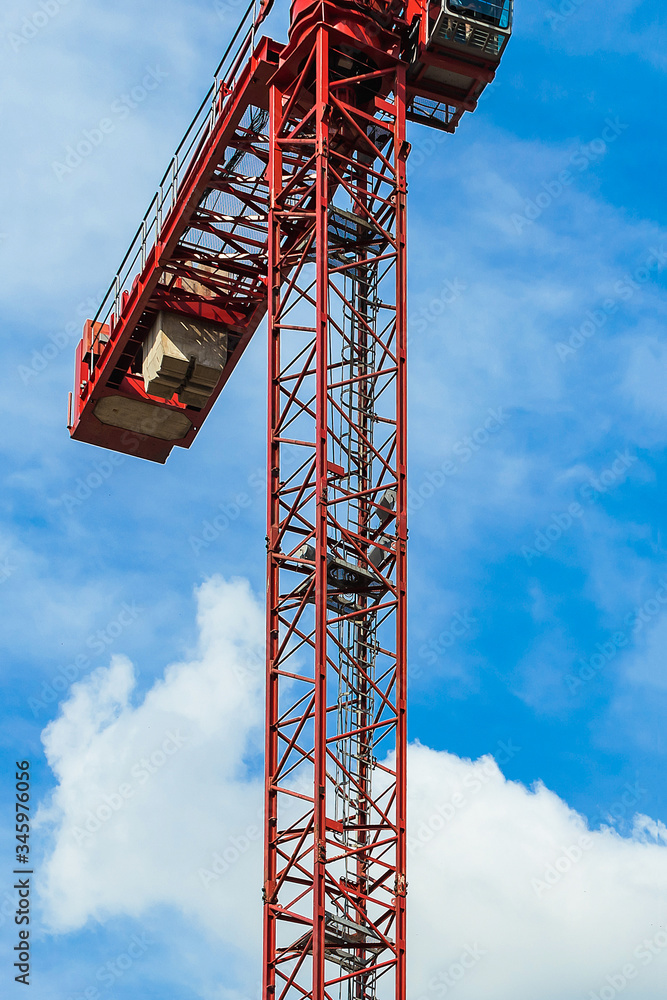 Red tower crane against blue sky with white clouds. Close up. Front shot. Copy space.