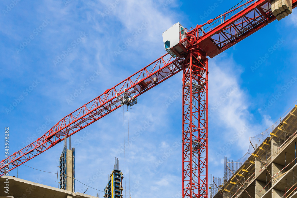 One high-rise crane against a house and sky during the construction phase. Industry concept for low-income young families. Mortgage, business, real estate loan. Summer. One high-rise crane against a house and sky during the construction phase. Industry concept for low-income young families. Mortgage, business, real estate loan. Summer.