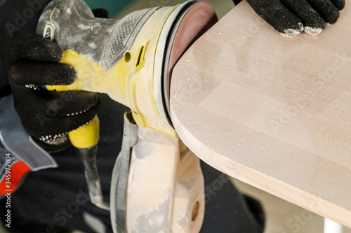 A young man, a carpenter polishes a wooden Board with an orbital sander. The concept of construction and repair