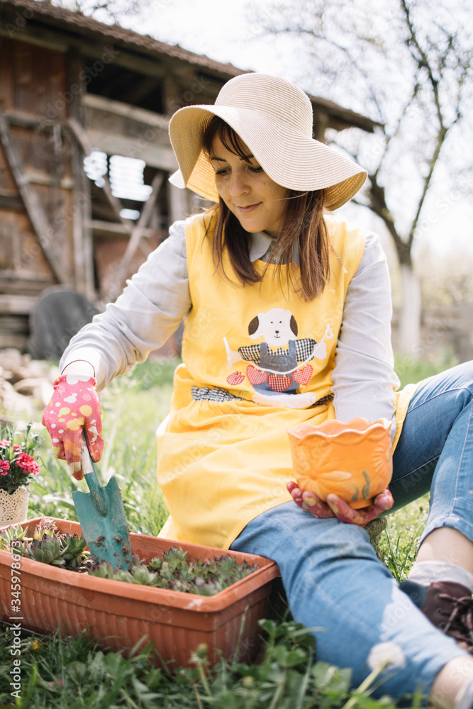 Obraz premium Female gardener holding hand shovel and pot while sitting on ground