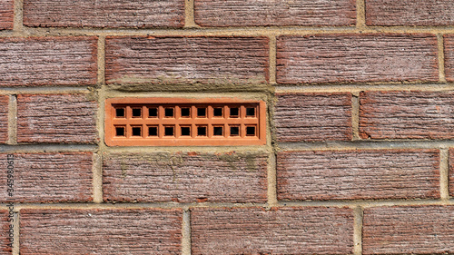 Terracotta coloured air brick embedded with a textured red brick wall.
