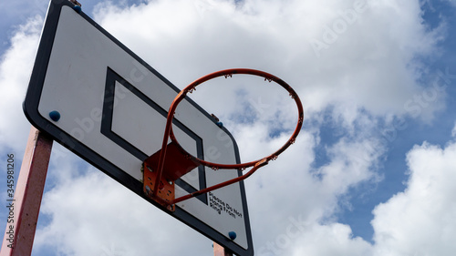 Outdoor Basketball hoop with white wooden backboard, black indication strips and faded red metal hoop and legs. © Anthony