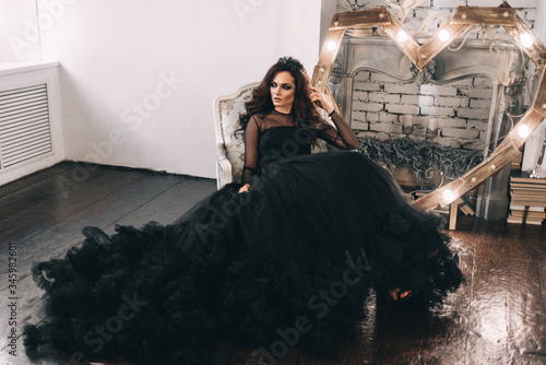 a beautiful girl in a black dress with brown hair poses in a photo Studio