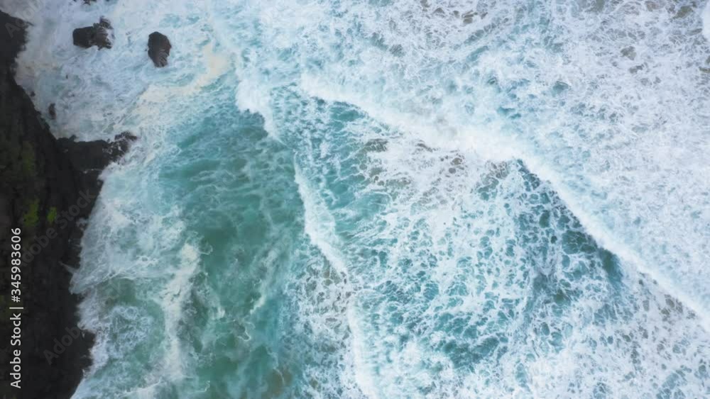 Aerial top view of the bubbling and foaming waves splashing near the coastal cliffs of the Hawaiian island. The coast is densely covered with plants. The tranquil landscape of a tropical paradise. 4K Aerial top view of the bubbling and foaming waves splashing near the coastal cliffs of the Hawaiian island. The coast is densely covered with plants. The tranquil landscape of a tropical paradise. 4K