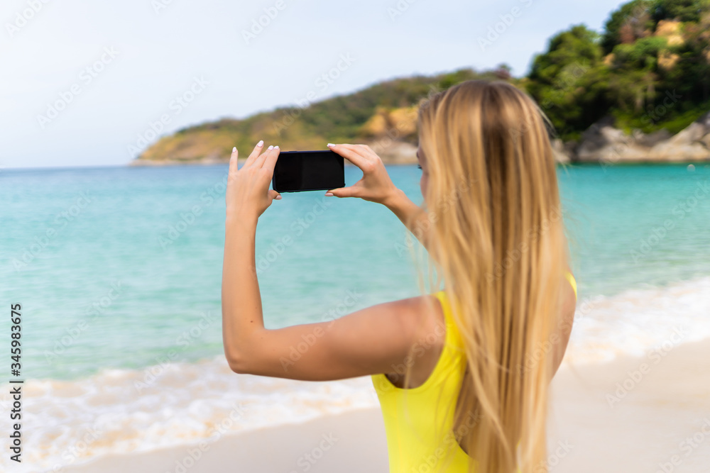 Back view of a young woman taking photograph with a smart phone camera on the beach Back view of a young woman taking photograph with a smart phone camera on the beach