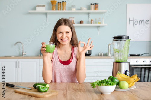 Sporty woman with glass of smoothie in kitchen at home
