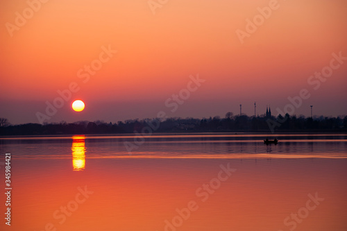 Beautiful sunset over the lake. Silhouettes of anglers in the boat. Lublin, Poland © diesirae
