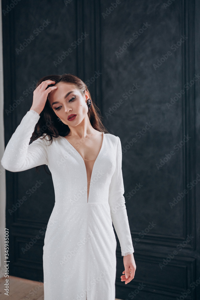 a beautiful bride in a white glittering wedding dress with brown hair poses in a photo Studio