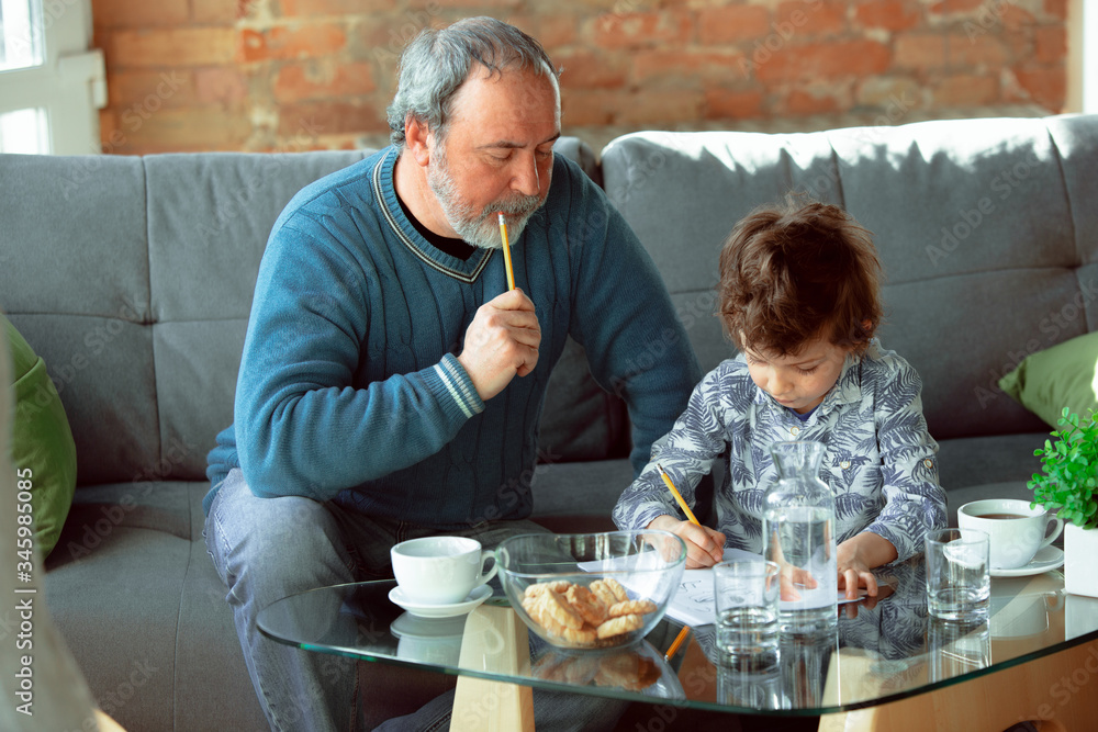 Useful time. Grandfather and his grandson spending time together insulated at home. Having fun, stadying, reading and drawing. Concept of quarantine, family, love, realtions, togetherness, education. Useful time. Grandfather and his grandson spending time together insulated at home. Having fun, stadying, reading and drawing. Concept of quarantine, family, love, realtions, togetherness, education.