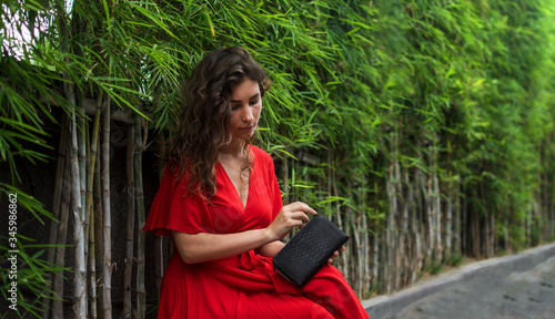 Trendy girl in nice clothes holds fashion snake leather clutch - Curly girl with exotic snakeskin python wallet. Handmade luxury purse from Bali island, Indonesia on natural bamboo background