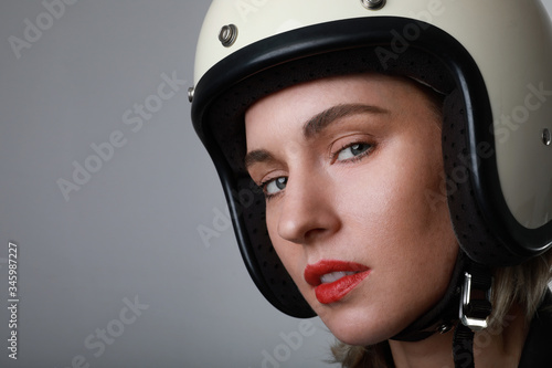 Close-up portrait of biker young woman, wearing white helmet, with red lips. Blue background. Space for your text. © face_reader_img