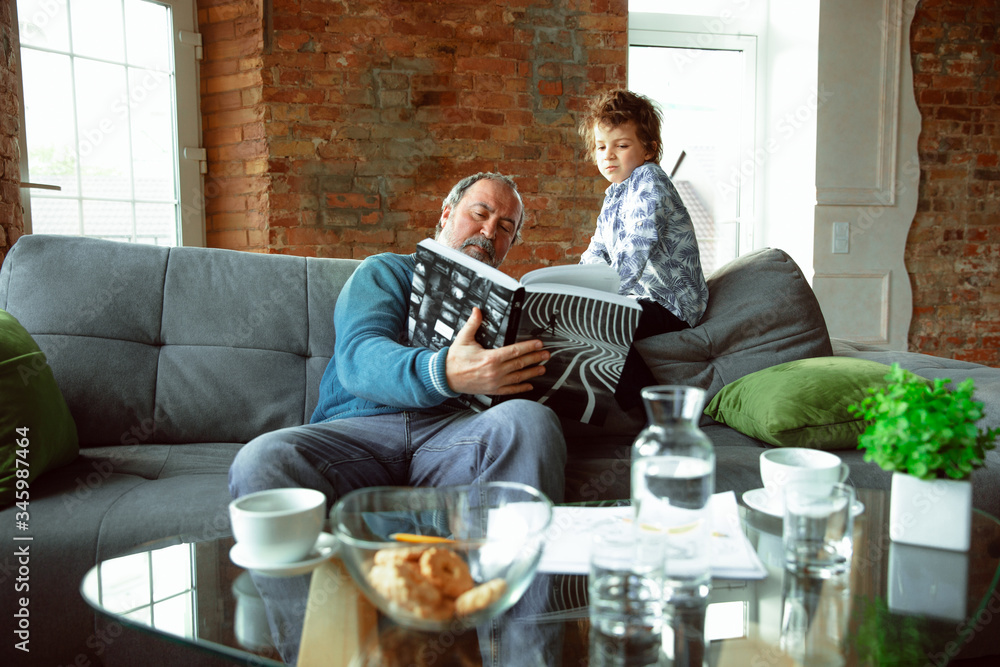 Coffee drinking. Grandfather and his grandson spending time together insulated at home. Having fun, reading magazine, happy. Concept of quarantine, family, love, realtions, togetherness, education. Coffee drinking. Grandfather and his grandson spending time together insulated at home. Having fun, reading magazine, happy. Concept of quarantine, family, love, realtions, togetherness, education.